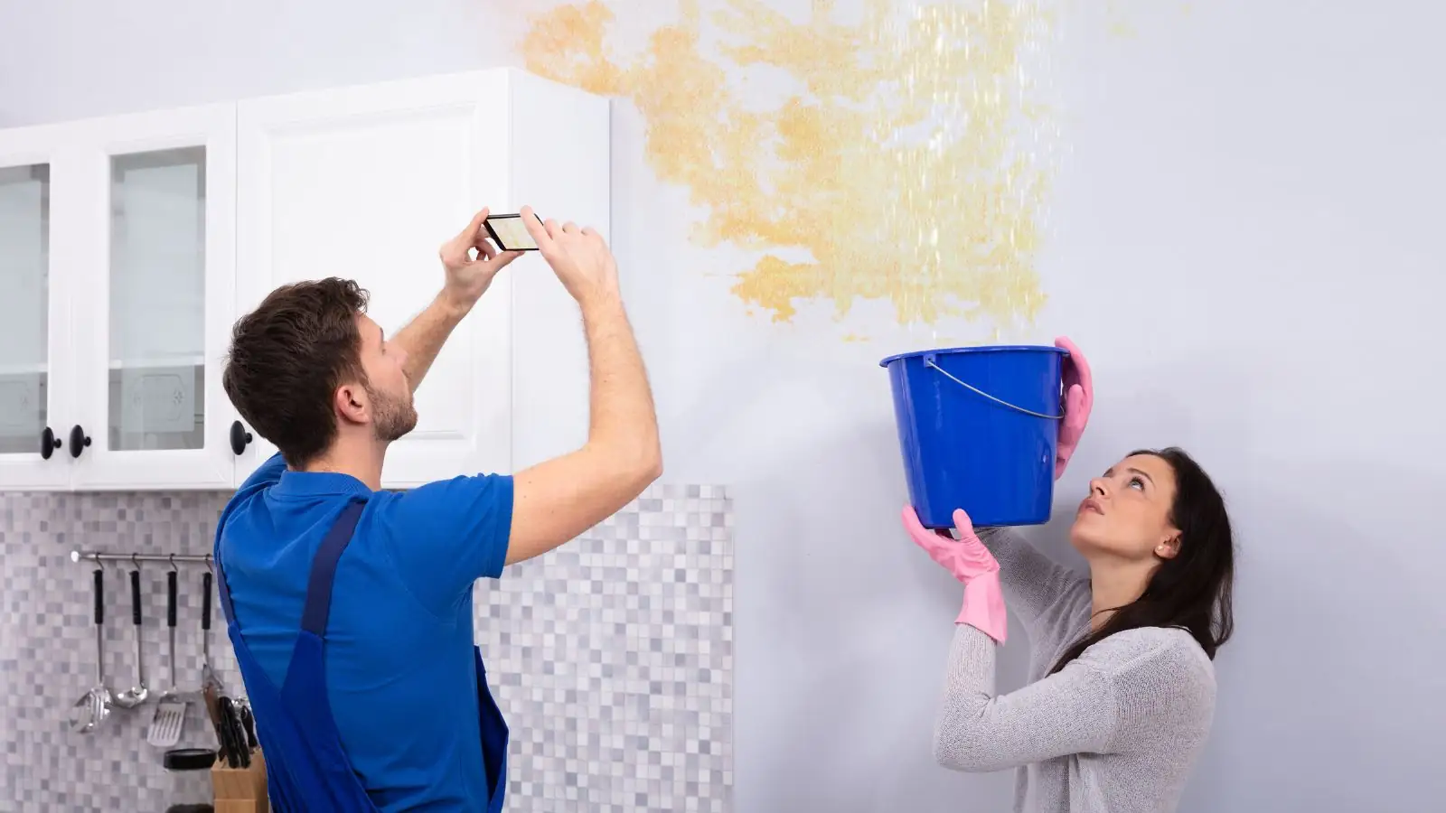 Renter and technician documenting a ceiling leak while a bucket catches water